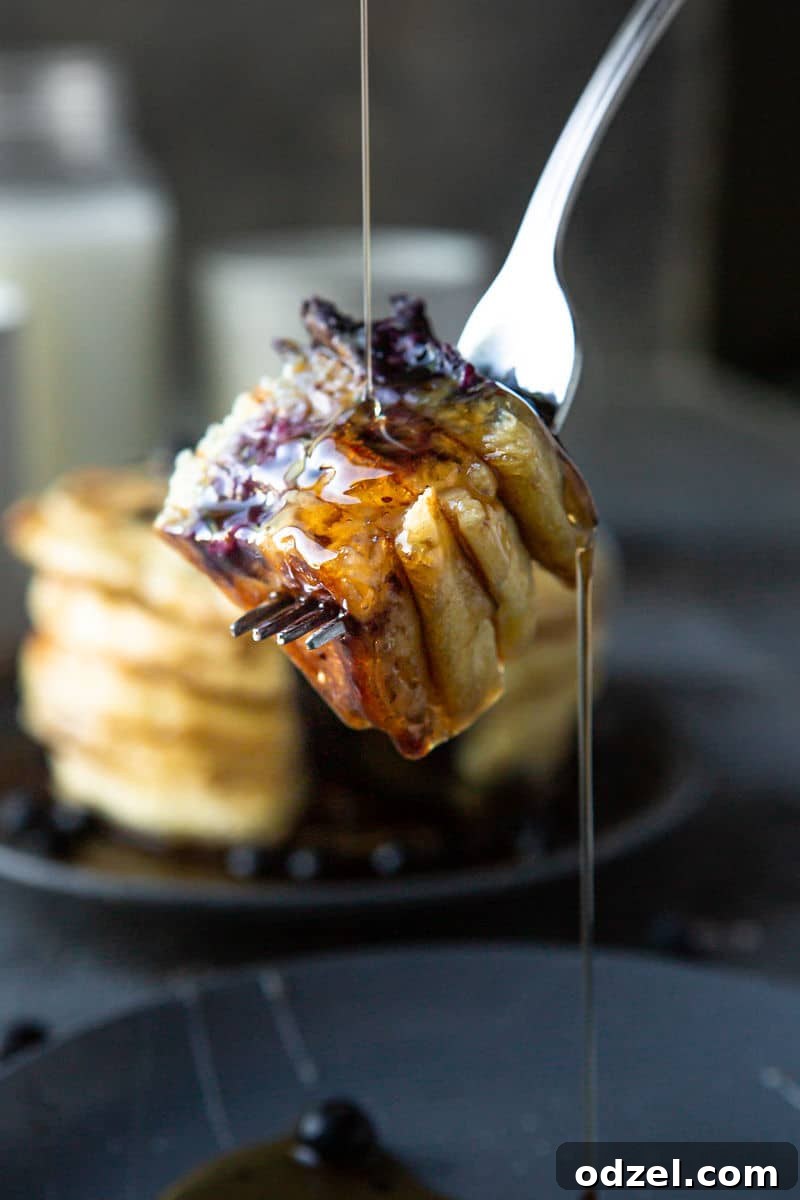 A fork holding four pieces of fluffy blueberry pancake, generously drizzled with maple syrup.