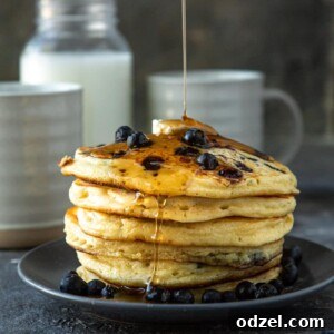A close-up of a stack of blueberry pancakes with butter and syrup, suggesting the final dish.