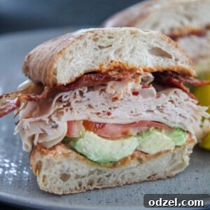Loaded Turkey Bacon Avocado Dream 7 Close-up of a turkey bacon avocado sandwich on a gray plate, showcasing the layers of fresh ingredients.