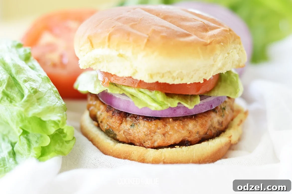 Zesty Salmon Burgers 6 Close-up of a salmon burger dressed with lettuce, onion, and tomato on a bun.