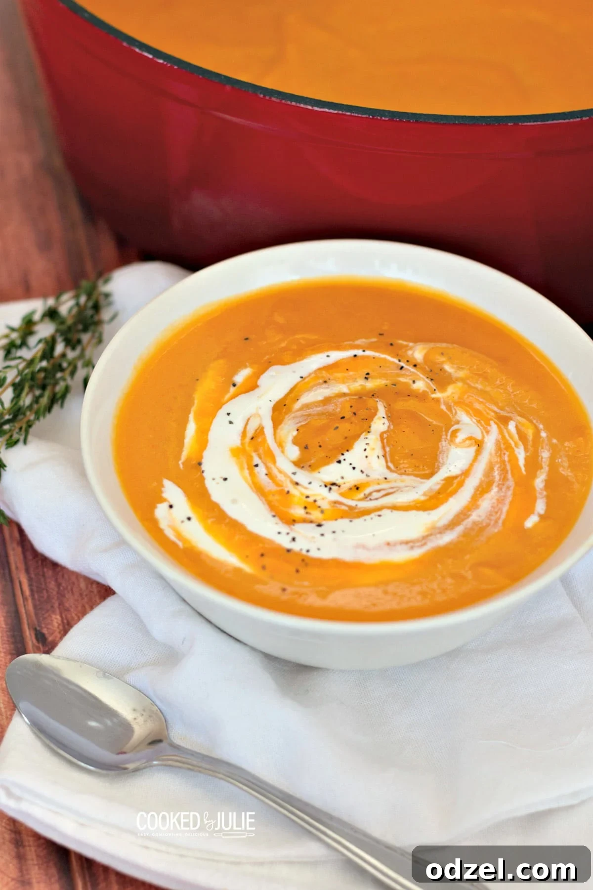 A bowl of creamy roasted butternut squash soup garnished with fresh herbs, with a spoon on the side.