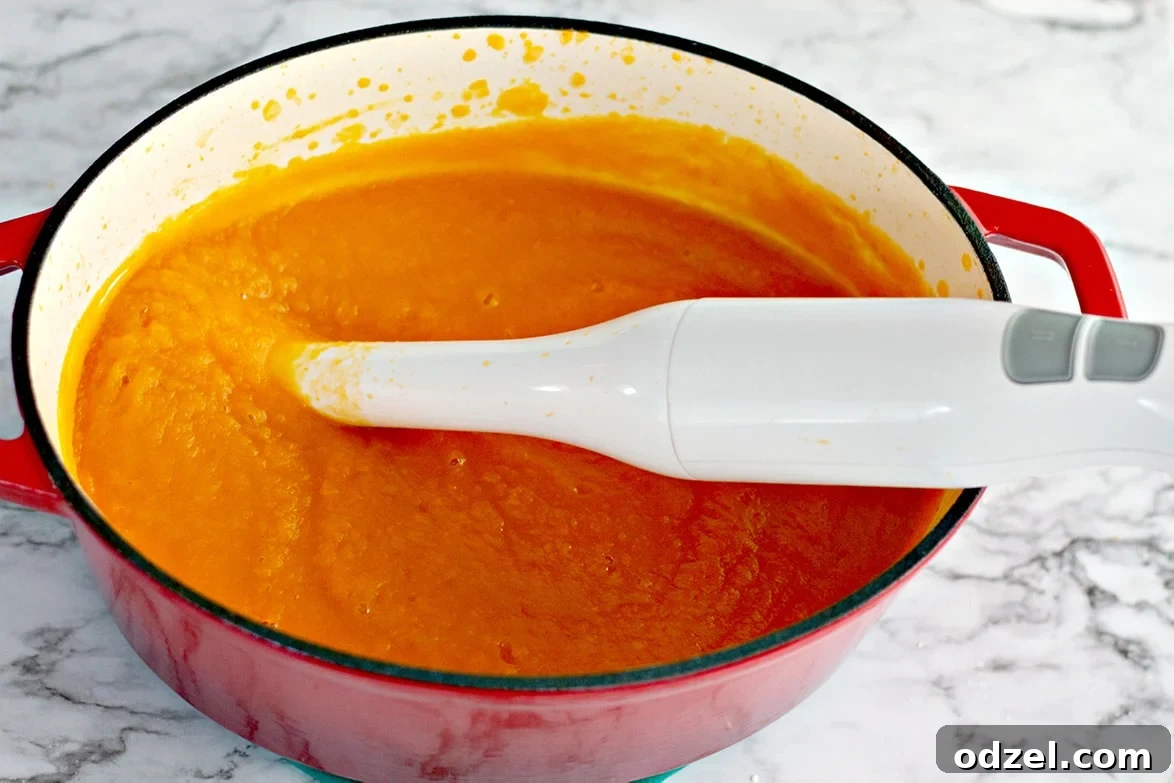 Creamy pureed butternut squash soup in a Dutch oven with an immersion blender resting inside.