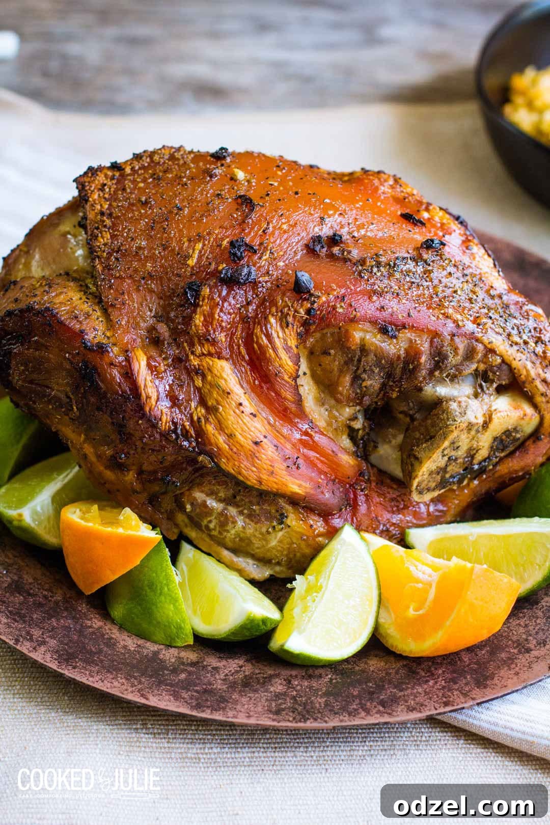 Cuban Pernil, a delicious slow-roasted pork shoulder with crispy skin, garnished with fresh limes and oranges on a rustic brown plate.