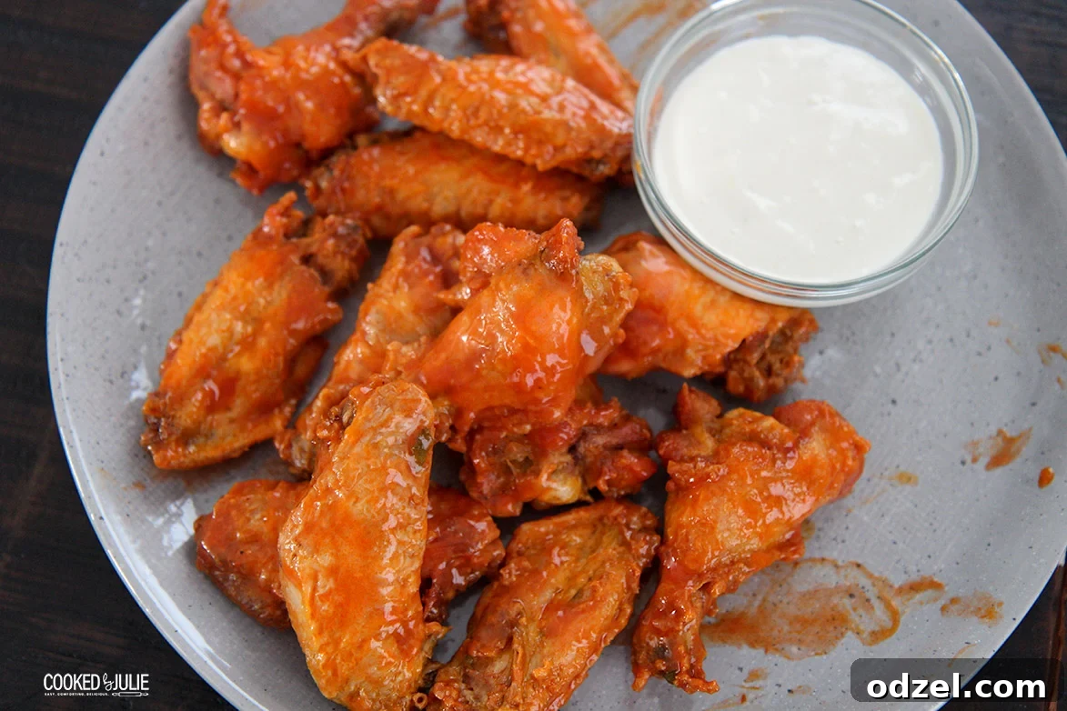 A close-up shot of perfectly sauced chicken wings resting on a gray plate, with a small bowl of creamy dipping sauce to the side.