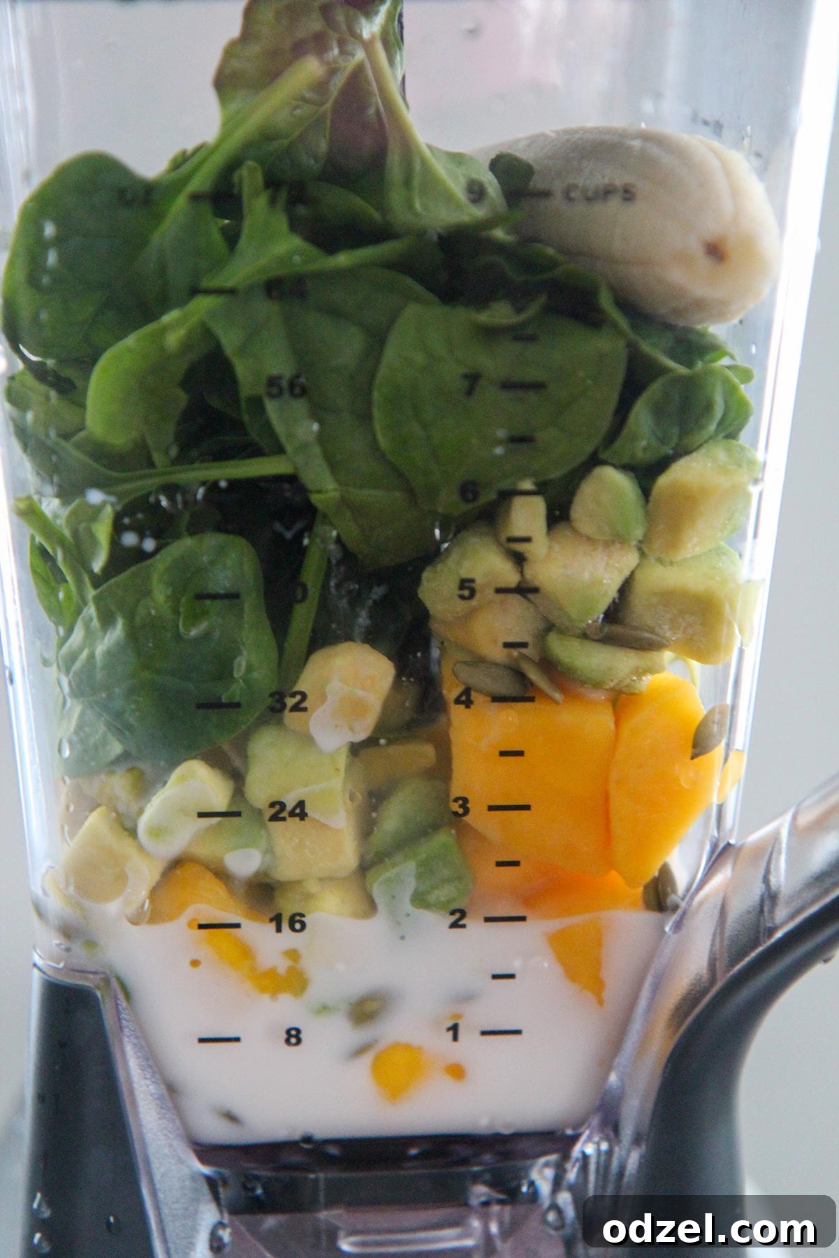 Fresh spinach, mango, banana, avocado, and almond milk ready to be blended in a powerful blender.