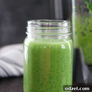Close-up of a Spinach Avocado Green Smoothie in a mason jar, topped with a few pumpkin seeds.