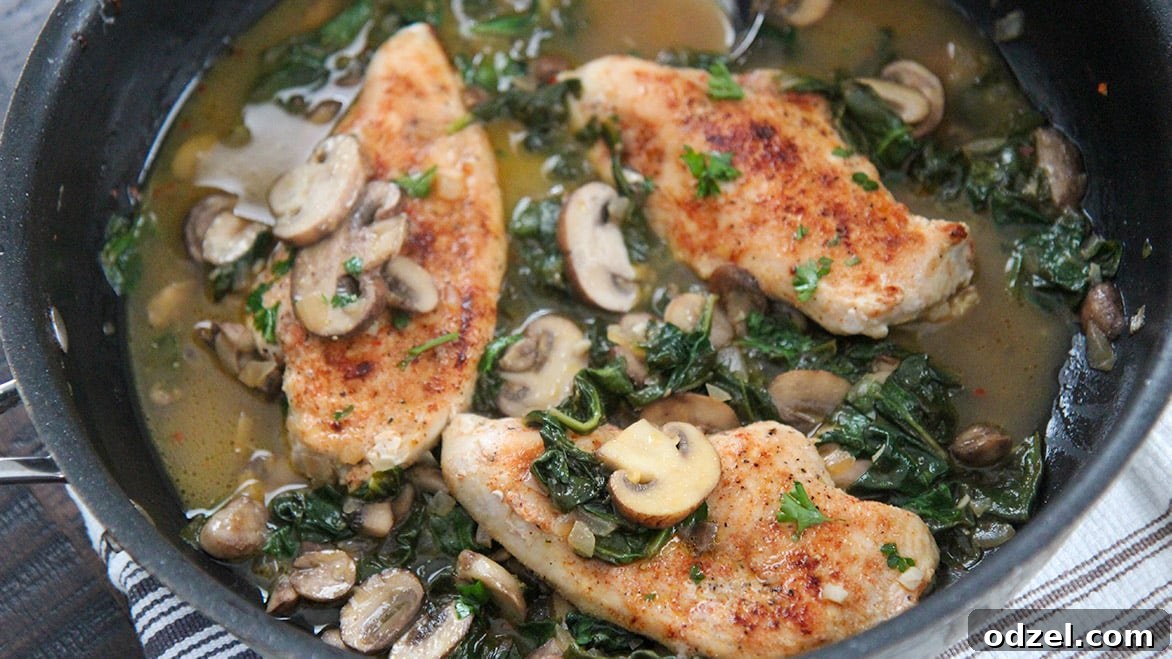 Close-up of a black skillet filled with golden chicken, sautéed mushrooms, wilted spinach, and a rich lemon-butter sauce.