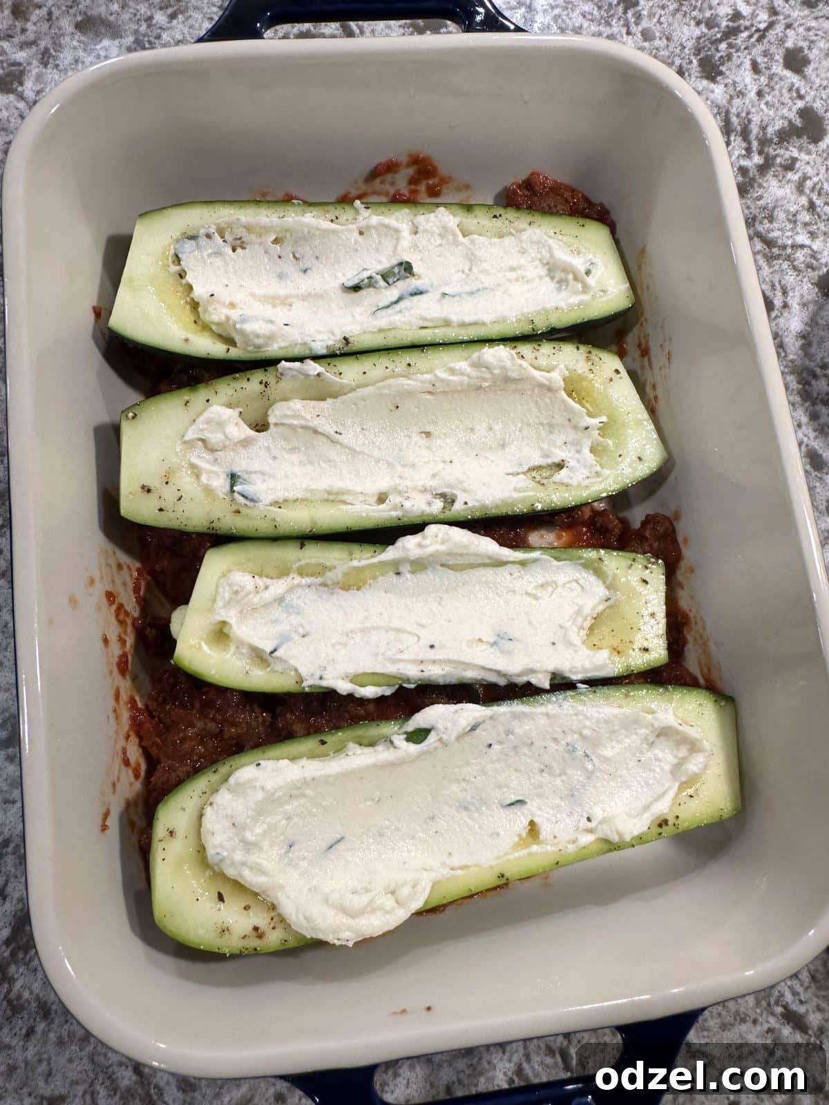 Four zucchini halves filled with creamy ricotta and rich meat sauce, before baking.