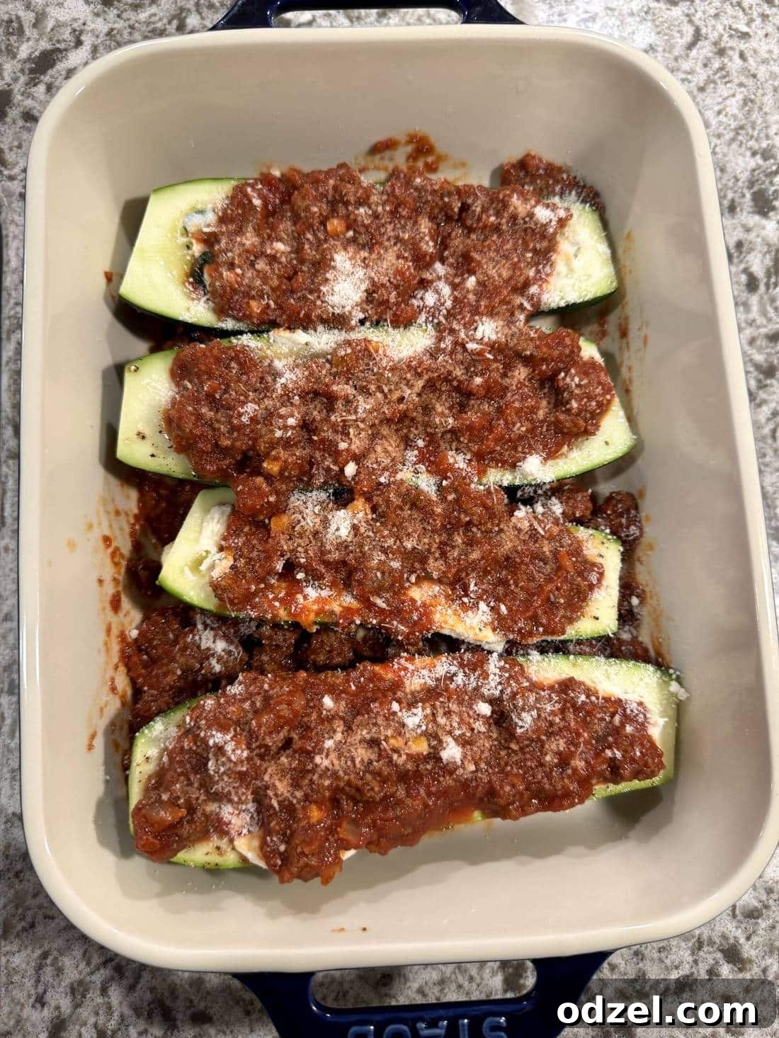 Four baked zucchini boats with golden brown cheese topping, meat sauce, and fresh parmesan cheese.