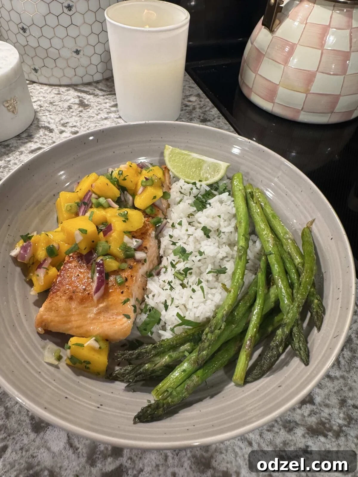 Cooked salmon topped with vibrant mango salsa, served alongside fluffy cilantro lime rice, tender asparagus, and a fresh lime wedge.