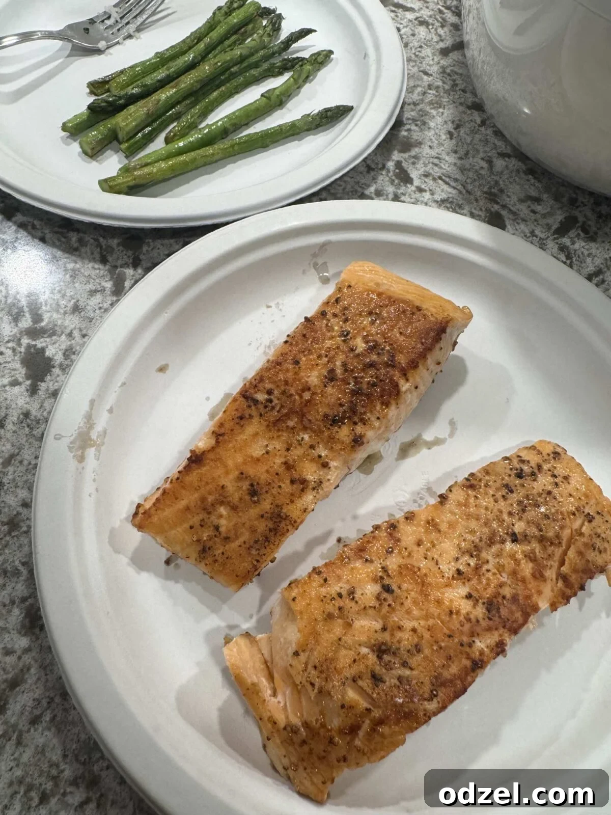 Two perfectly cooked salmon fillets on one plate, accompanied by a side of tender, vibrant green asparagus.