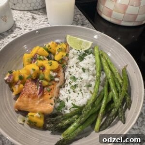 Cooked salmon topped with mango salsa, served with rice, asparagus, and a lime wedge.
