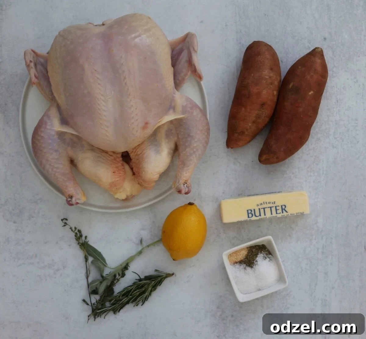 Raw ingredients for spatchcock chicken and sweet potatoes: a whole chicken, sliced sweet potatoes, spices, butter, lemon, and fresh herbs.