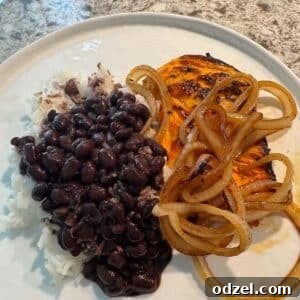 Grilled chicken with onions on top with a side of rice and black beans.