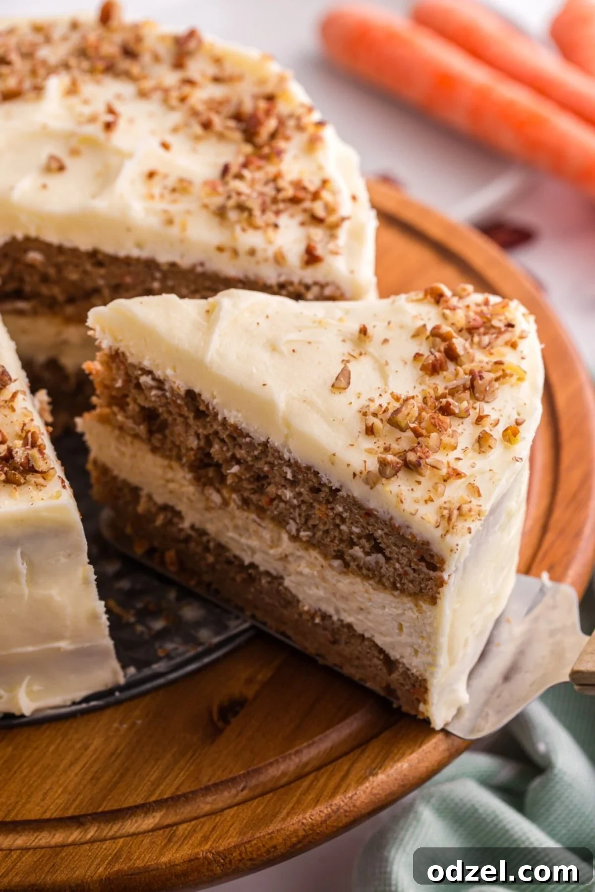 Layered carrot cake cheesecake with cream cheese frosting and chopped pecans on a wooden cake stand.