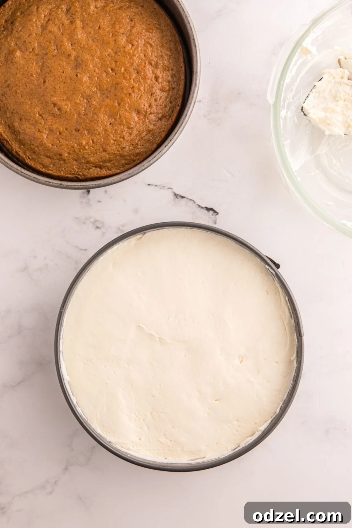 Baked cheesecake layer in a springform pan with carrot cake layer and cream cheese frosting on the side.