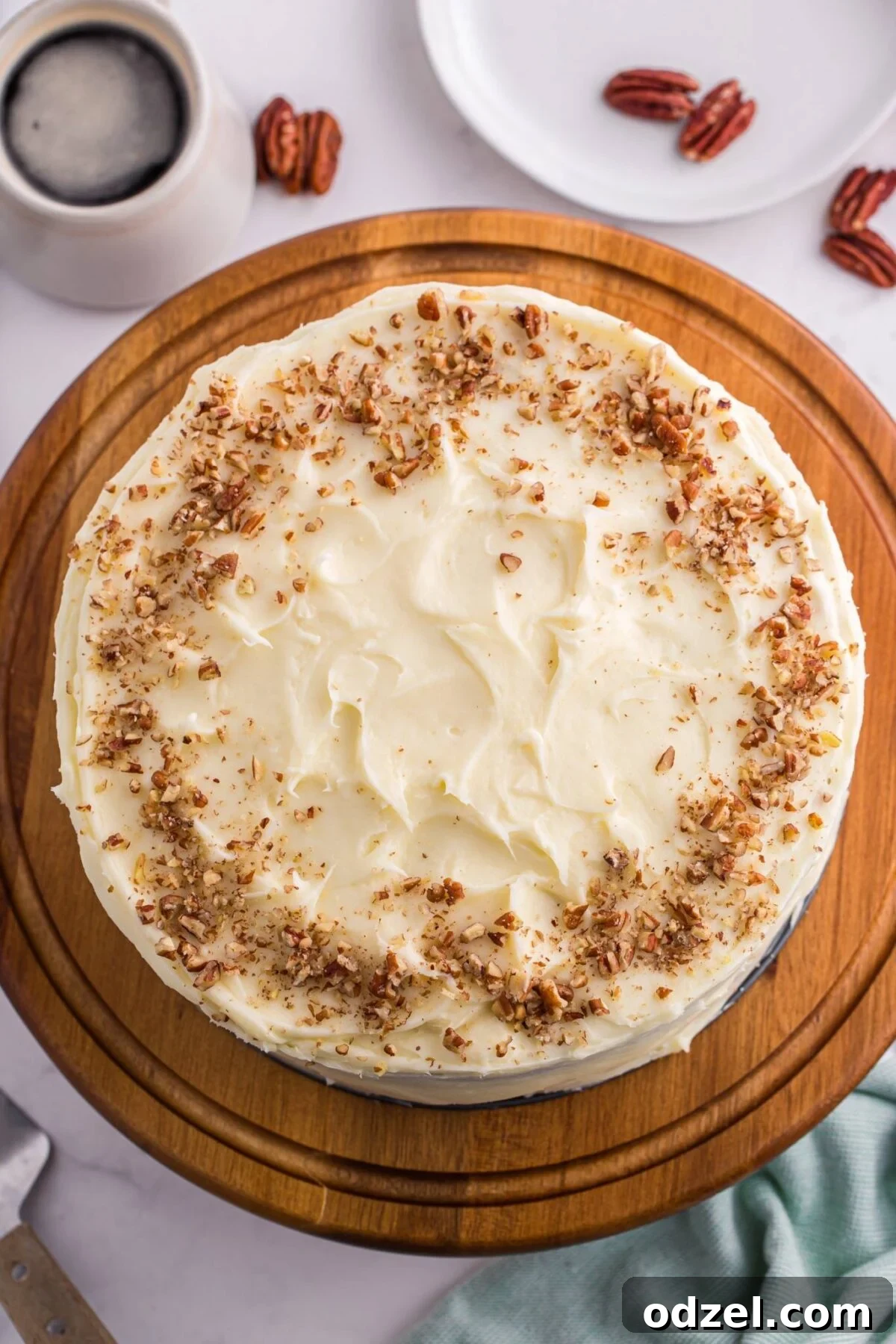 Carrot cake cheesecake topped with cream cheese frosting and chopped pecans on a wooden cake stand.