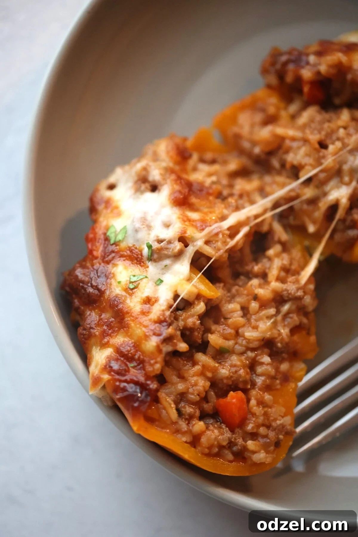 Savory Stuffed Bell Peppers 2 One cheesy stuffed bell pepper, cut in half to reveal the savory filling of ground beef and rice, topped with perfectly melted cheese, with a fork poised for a bite.