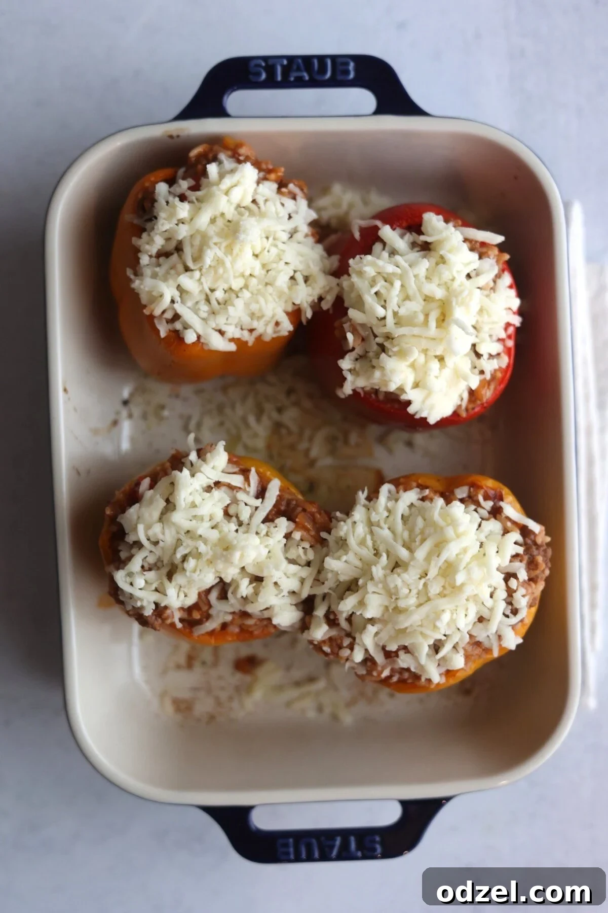 Savory Stuffed Bell Peppers 5 Four stuffed peppers with a generous layer of shredded white cheese on top, ready for baking.
