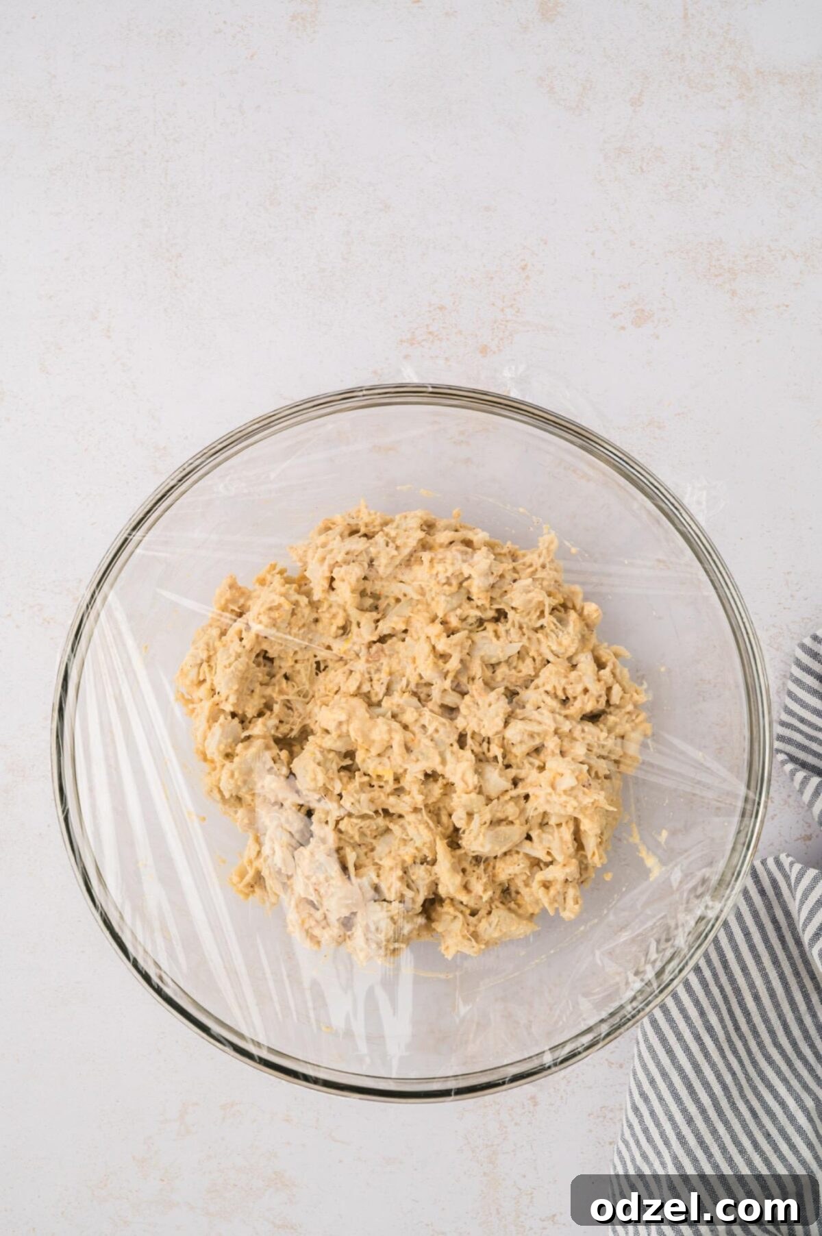 Crab cake mixture in a glass bowl with plastic wrap on top. 