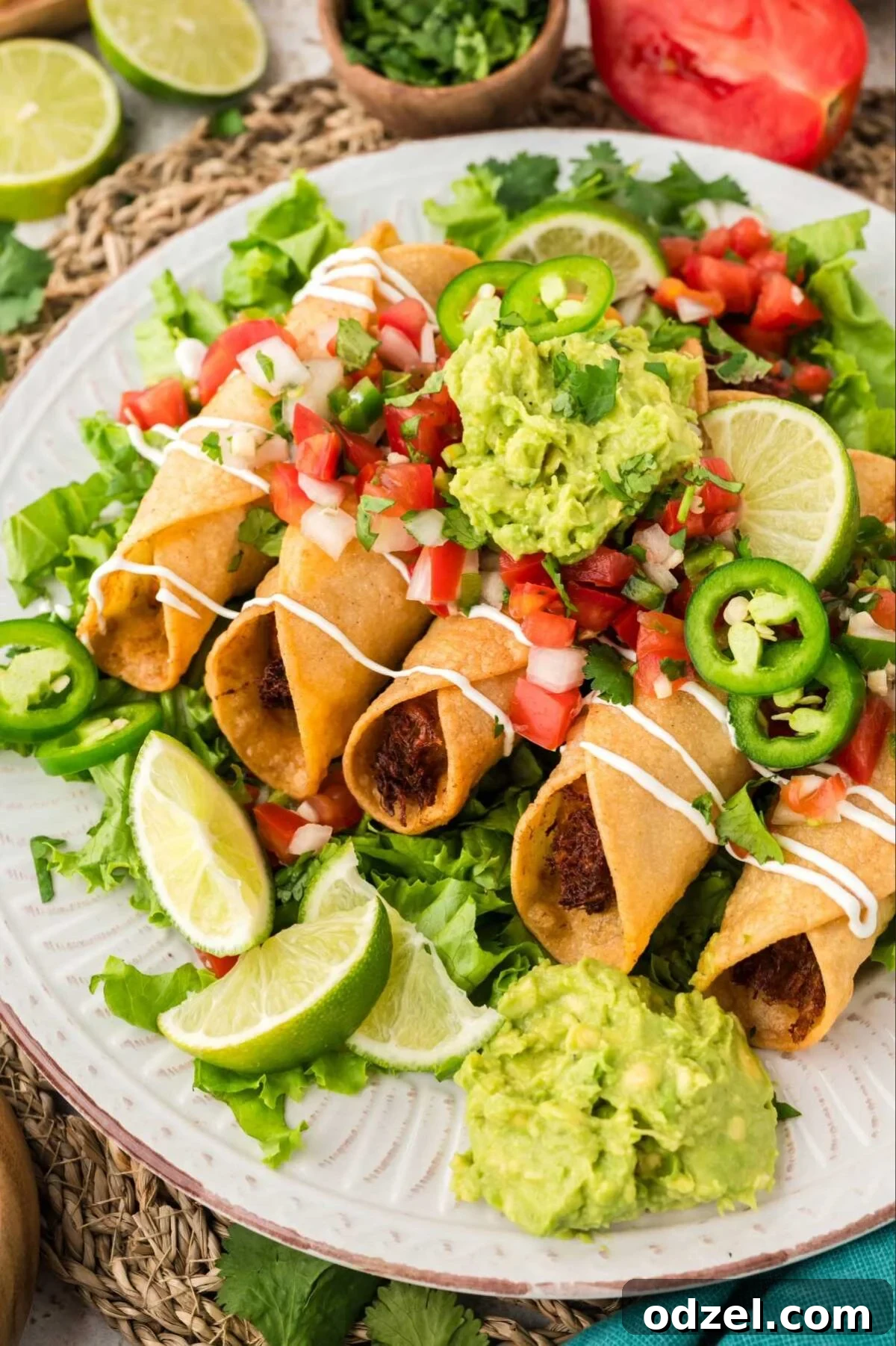 Smoky Chipotle Chicken Flautas 2 Chicken flautas on a plate with guacamole, pico de Gallo, jalapeños, and lime wedges,