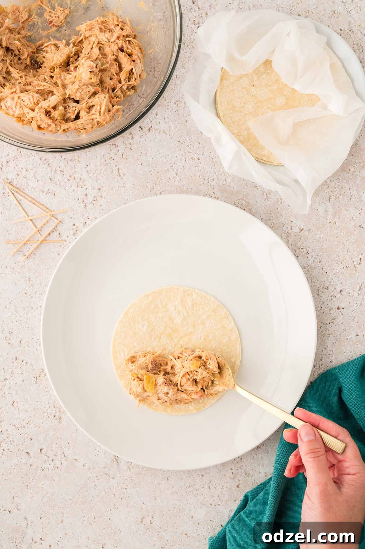 Smoky Chipotle Chicken Flautas 5 a hand placing shredded chicken mixture on a tortilla.