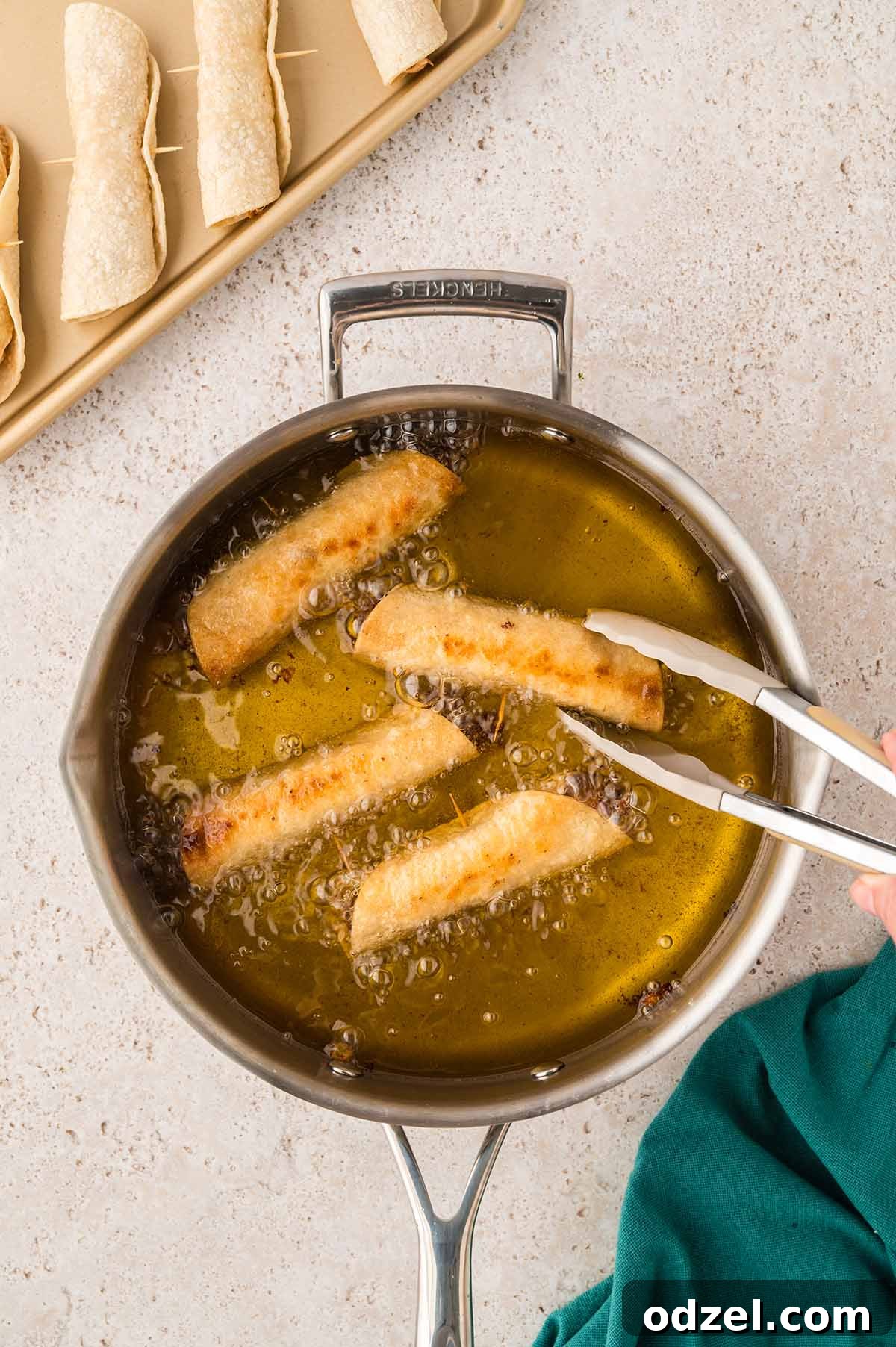 Smoky Chipotle Chicken Flautas 7 chicken flautas frying in a skillet with a tong.