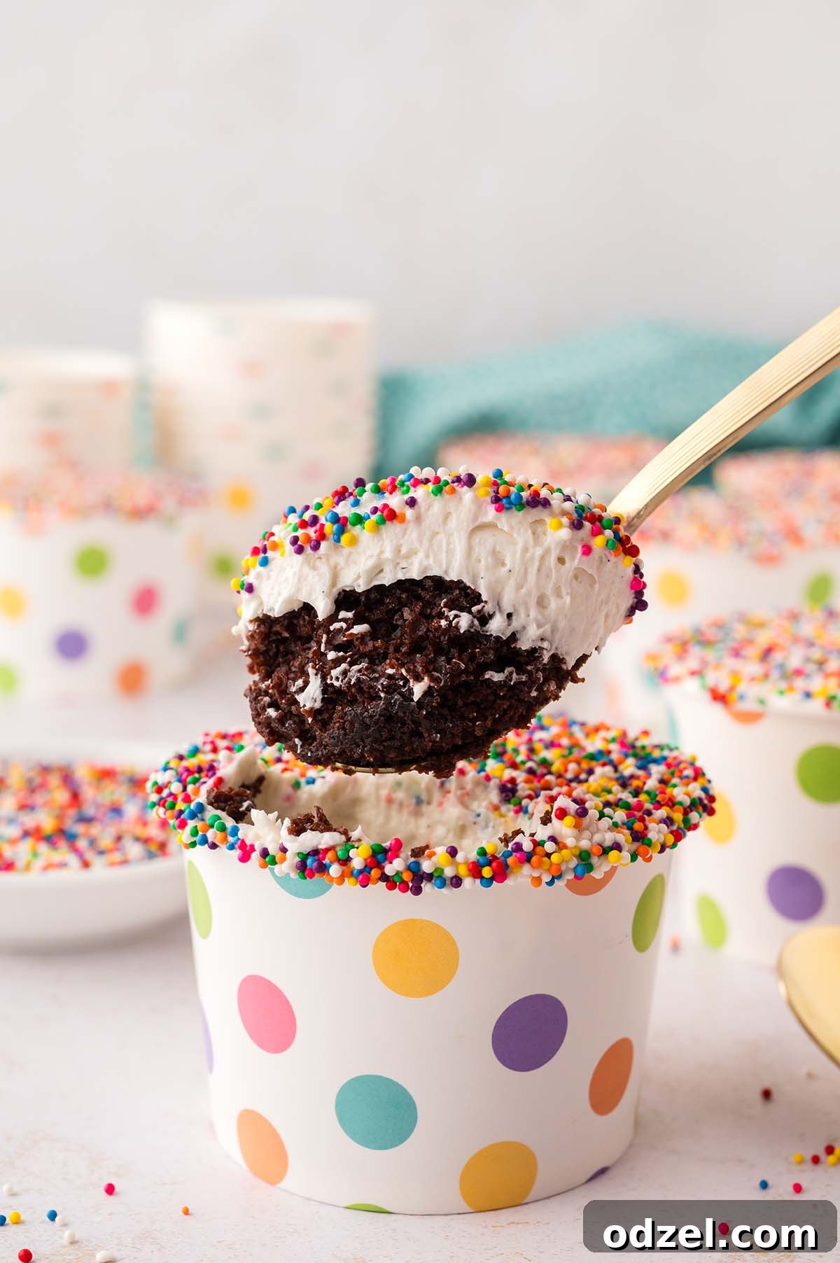 Copycat Dot Cakes Recipe: Make Classic Mini Cake Bites at Home 3 Spoon lifting a chocolate dot cake cup topped with vanilla frosting and rainbow sprinkles.