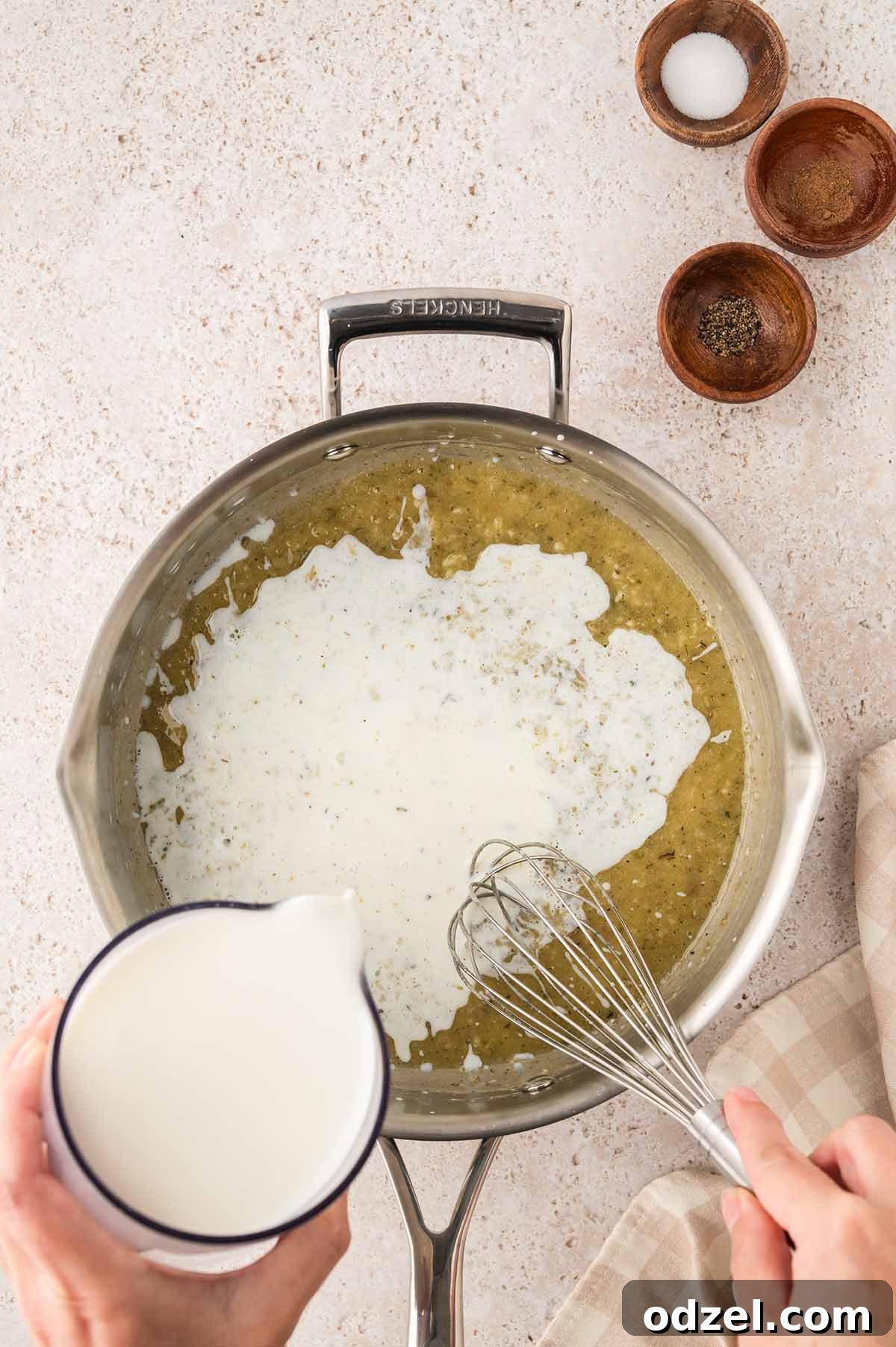 Creamy Pesto Chicken Lasagna Recipe 6 Hand pouring milk into a skillet with butter and flour while whisking to make a béchamel sauce.