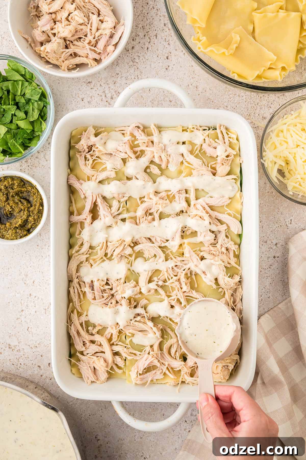 Creamy Pesto Chicken Lasagna Recipe 8 Sauce being poured over the lasagna layers.