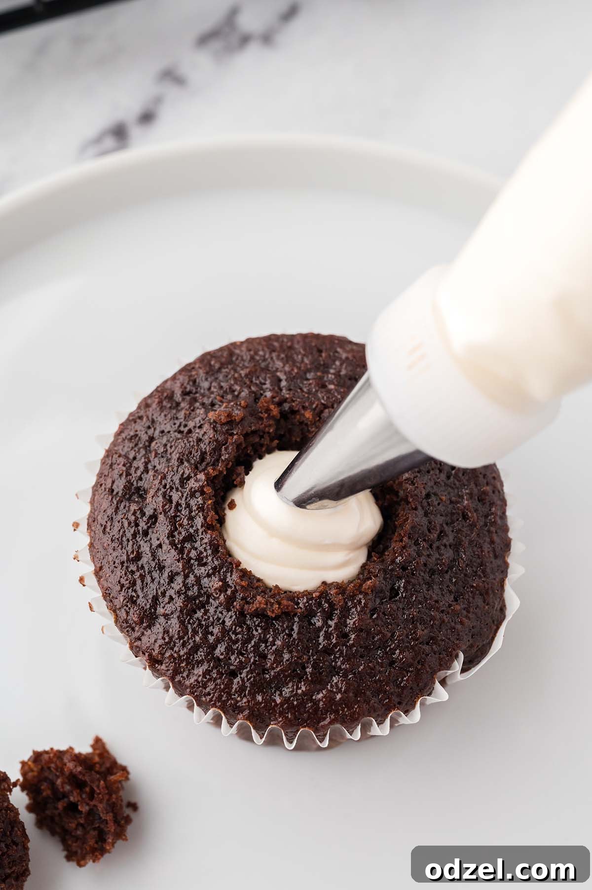 Gooey Marshmallow-Filled Chocolate Cupcakes 5 a piping bag filling the center of a cupcake.