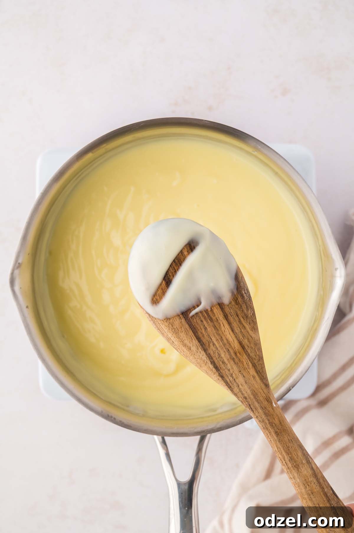 Southern Classic Banana Pudding Recipe 6 thick yellow custard in a saucepan with a wooden spoon.