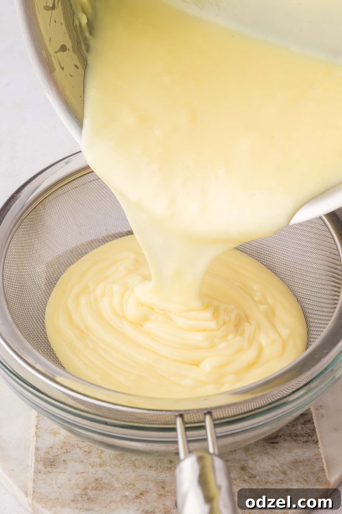 Southern Classic Banana Pudding Recipe 7 yellow custard going through a mesh sieve.