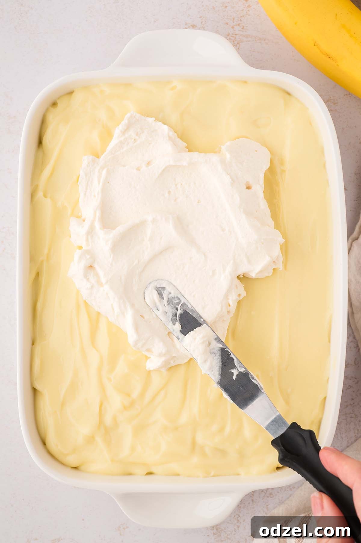 Southern Classic Banana Pudding Recipe 9 Whipped cream being evenly spread over the banana pudding.