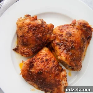 three baked chicken thighs on a white plate with a gray and white towel on the side.