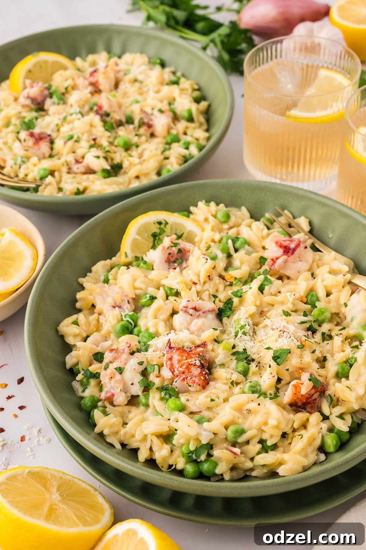Creamy Lemon Garlic Lobster Orzo Recipe 8 two green bowls filled with lobster orzo and lemon wedges and drinks on the side.