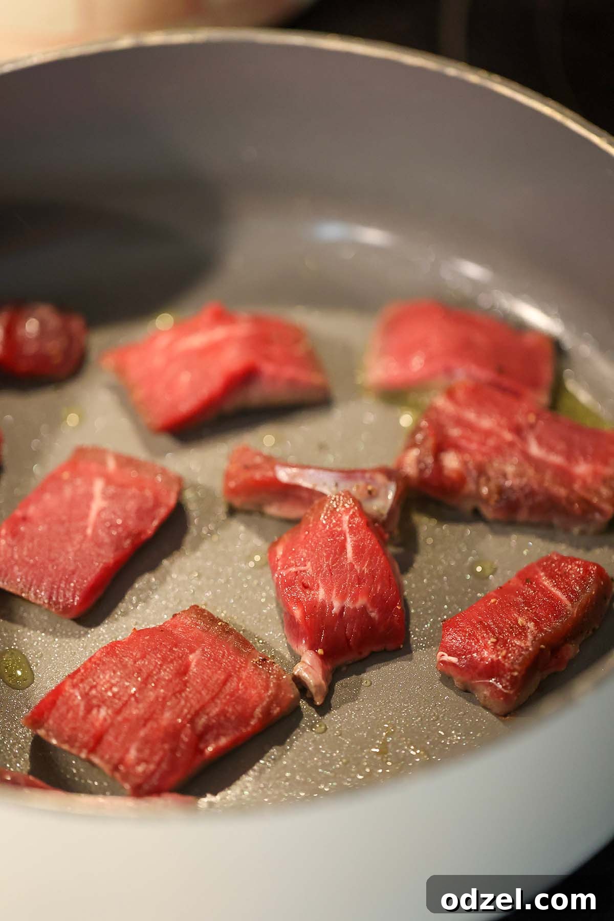 steak pieces cooking in a skillet.
