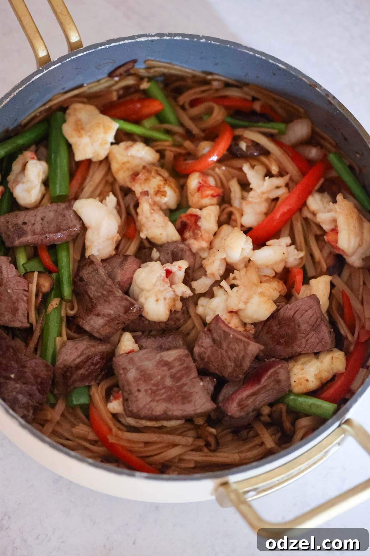 noodles in a skillet with lobster and steak on top.
